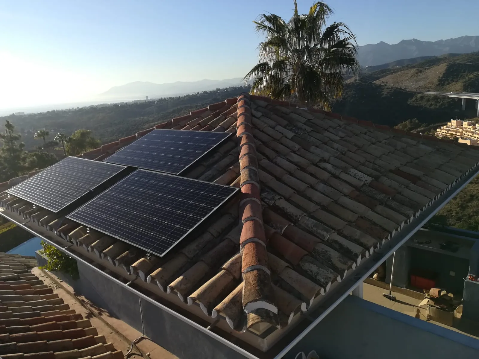 Placas solares instaladas por Aula Solar sobre un tejado de teja con vistas al mar y a la montaña